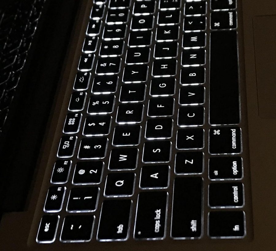 A Macbook keyboards backlighting stands out compared to dark, nighttime surroundings. 