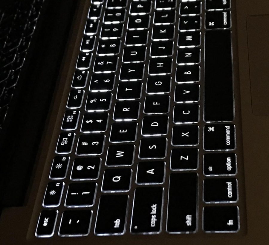 A Macbook keyboard's backlighting stands out compared to dark, nighttime surroundings. 