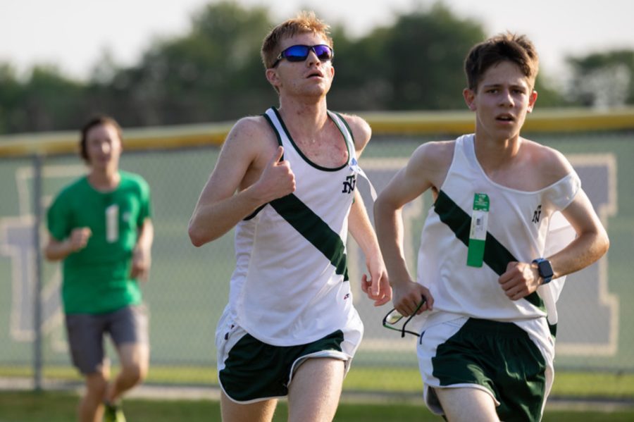Green, left, outfitted in New Trier gear and blue sunglasses, runs neck and neck with a fellow Trevian runner