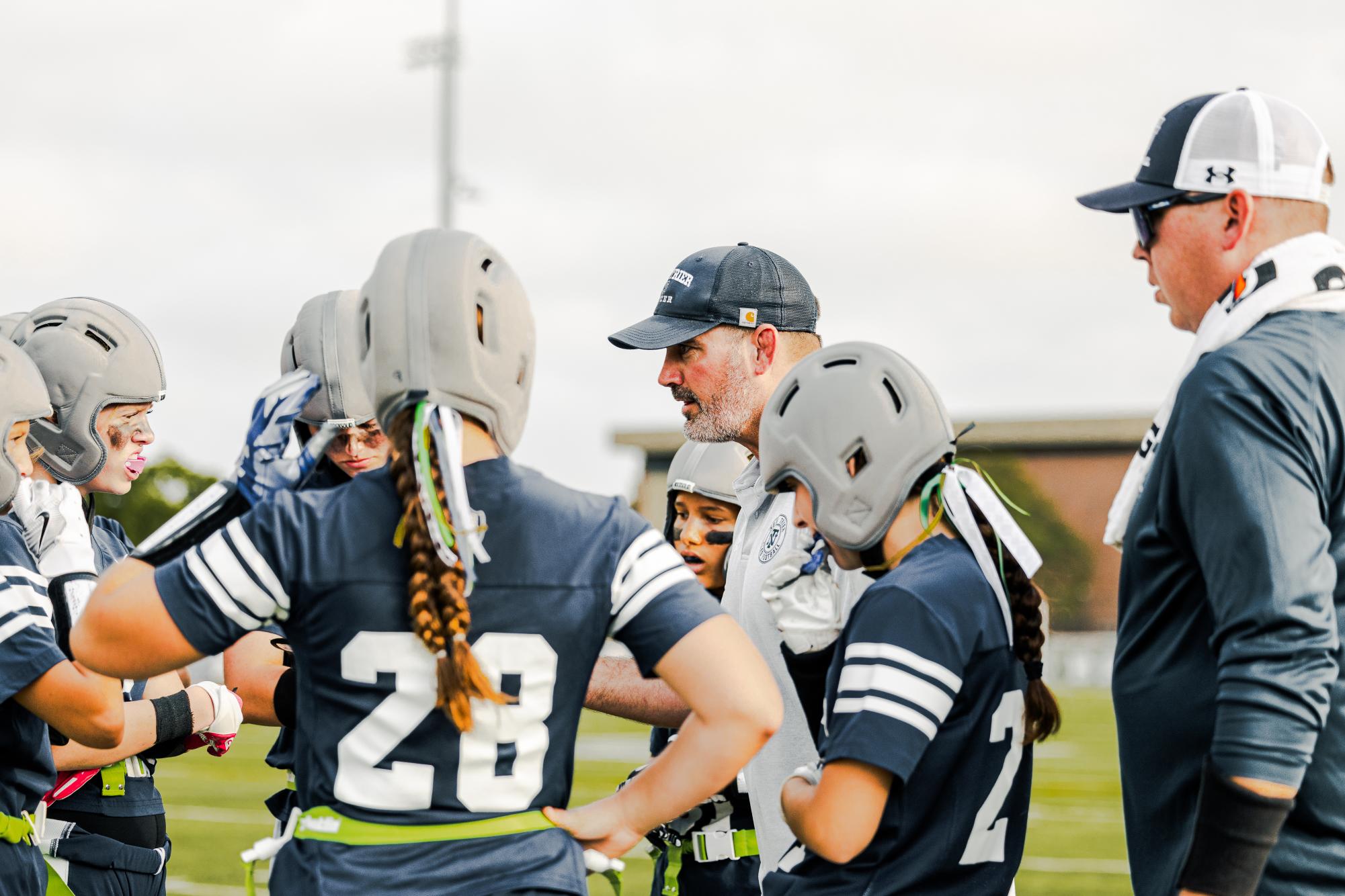 Girls flag football team gathers for a huddle led by head coach Mark Colegrove